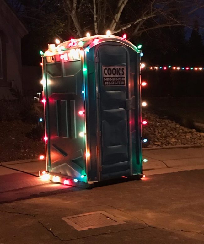 Um banheiro químico para canteiros de obras decorado com luzes de Natal coloridas, é Natal para todos